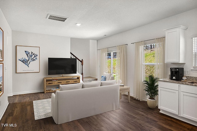 living room featuring dark wood-style floors, baseboards, visible vents, and a textured ceiling