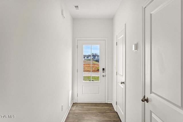 doorway with dark wood-style floors, visible vents, and baseboards