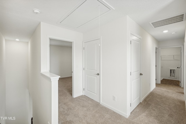 hallway with light colored carpet, visible vents, baseboards, an upstairs landing, and attic access