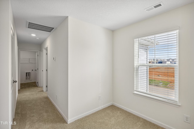 hall featuring light carpet, baseboards, visible vents, and a textured ceiling