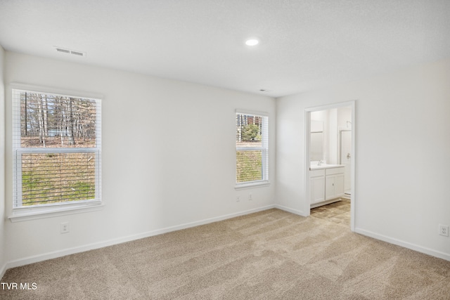 unfurnished bedroom with light carpet, ensuite bath, visible vents, and baseboards