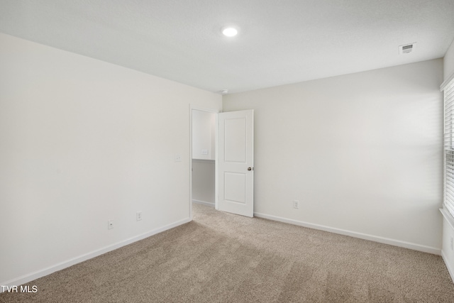 empty room with carpet, visible vents, and baseboards