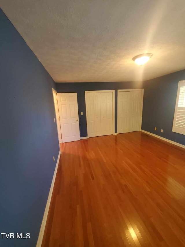 unfurnished bedroom featuring multiple closets, hardwood / wood-style floors, and a textured ceiling