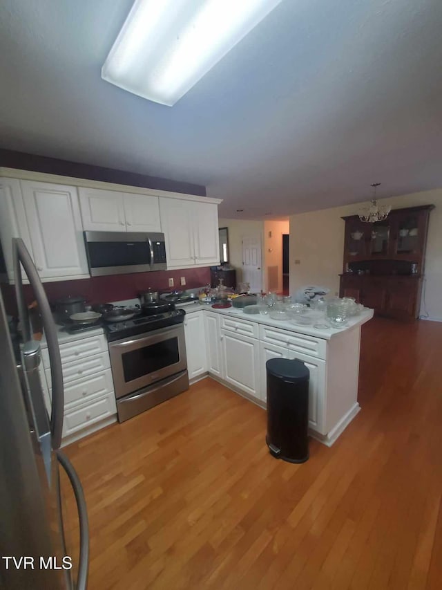 kitchen with light wood-type flooring, kitchen peninsula, stainless steel appliances, white cabinets, and a chandelier