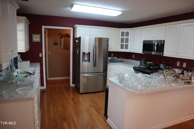 kitchen with sink, light wood-type flooring, kitchen peninsula, stainless steel appliances, and white cabinets