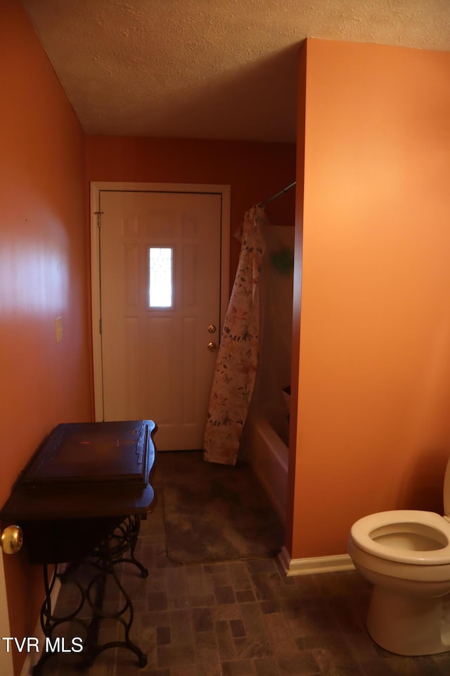 bathroom with shower / bath combination with curtain, toilet, and a textured ceiling