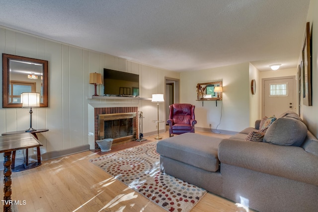 living room featuring a textured ceiling, light wood-type flooring, and a brick fireplace