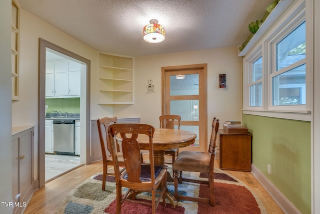 dining area with built in features, a textured ceiling, and light hardwood / wood-style floors