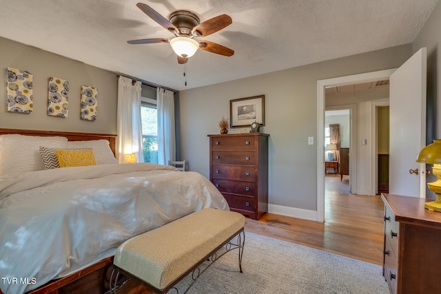 bedroom with a textured ceiling, light wood-type flooring, and ceiling fan