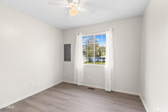 empty room featuring ceiling fan, electric panel, light hardwood / wood-style flooring, and a textured ceiling