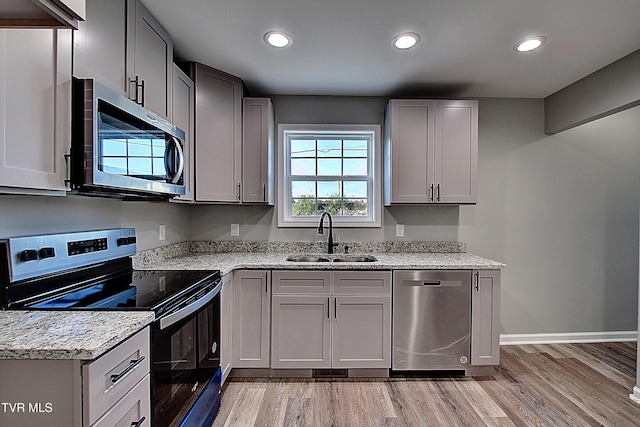 kitchen featuring light stone counters, sink, stainless steel appliances, and light hardwood / wood-style floors