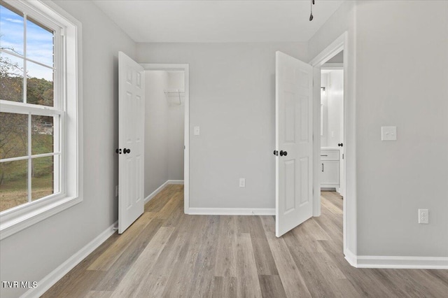 unfurnished bedroom featuring a closet, multiple windows, a walk in closet, and light hardwood / wood-style flooring