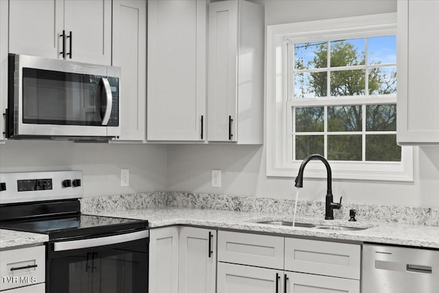 kitchen with white cabinets, stainless steel appliances, light stone countertops, and sink