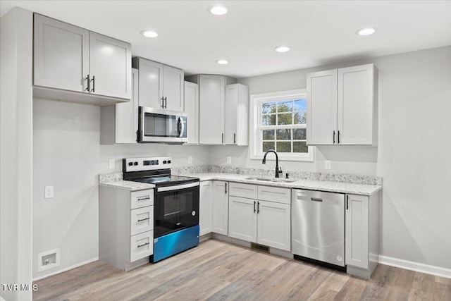 kitchen featuring light stone counters, sink, stainless steel appliances, and light wood-type flooring