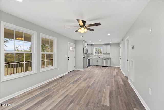 unfurnished living room with ceiling fan, sink, and light wood-type flooring