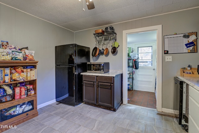 kitchen featuring wood walls, ceiling fan, dark brown cabinets, and black fridge