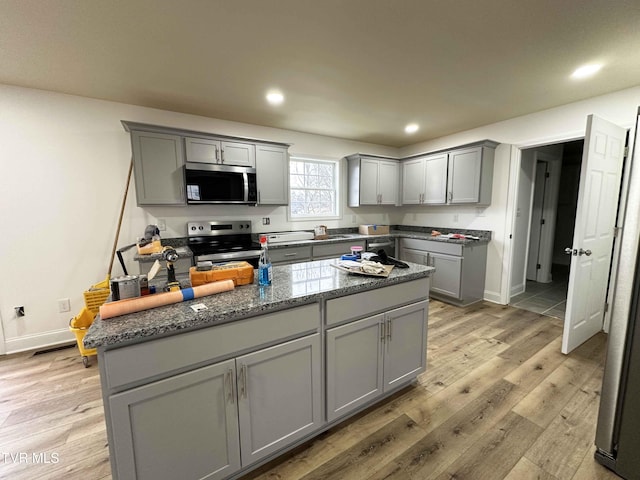 kitchen with a center island, light wood-type flooring, dark stone countertops, appliances with stainless steel finishes, and gray cabinets