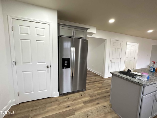 kitchen with gray cabinetry, stainless steel fridge with ice dispenser, dark wood-type flooring, and stone counters