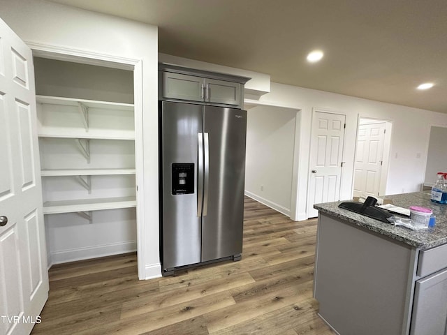 kitchen with dark stone countertops, dark hardwood / wood-style flooring, gray cabinetry, and stainless steel refrigerator with ice dispenser