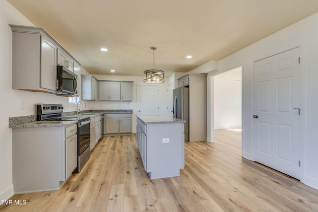 kitchen with light stone counters, light wood finished floors, a sink, gray cabinetry, and stainless steel appliances