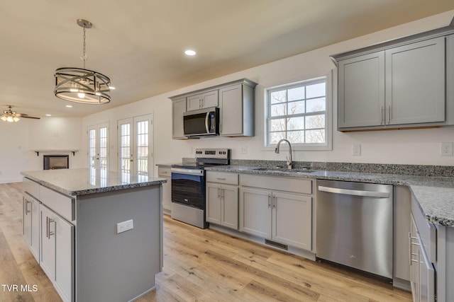 kitchen featuring a kitchen island, a sink, gray cabinetry, stainless steel appliances, and light wood-style floors