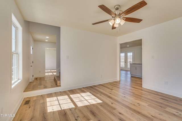 empty room featuring stairway, a ceiling fan, baseboards, visible vents, and light wood finished floors