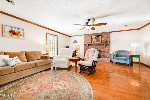 living room with ceiling fan, a textured ceiling, light wood-type flooring, ornamental molding, and a fireplace