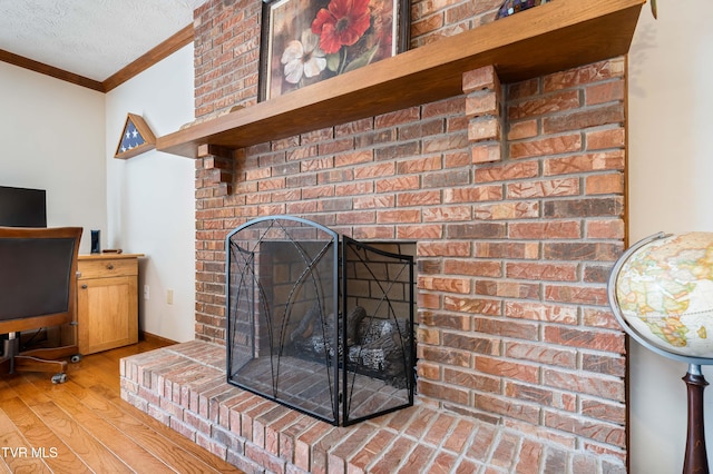 details with crown molding, wood-type flooring, a textured ceiling, and a brick fireplace