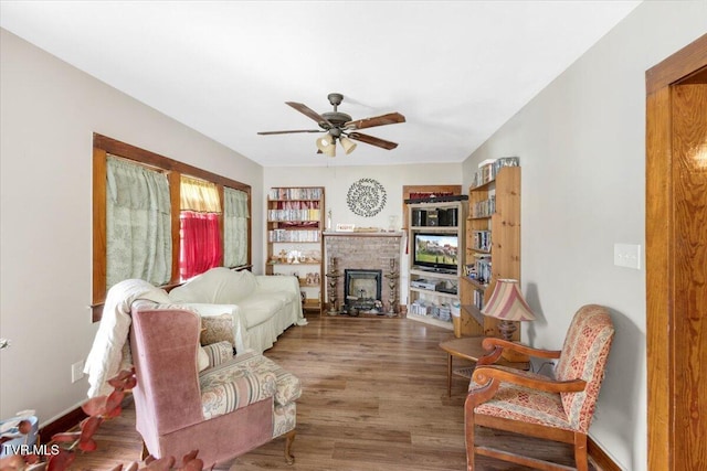 living room featuring wood-type flooring, ceiling fan, and a brick fireplace