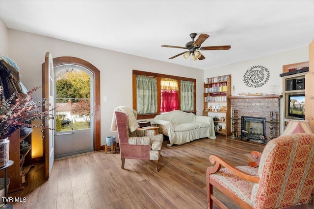 living room with hardwood / wood-style flooring, a brick fireplace, and ceiling fan