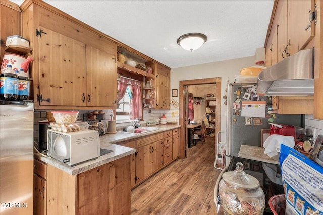 kitchen featuring extractor fan, stainless steel refrigerator, tasteful backsplash, sink, and light wood-type flooring