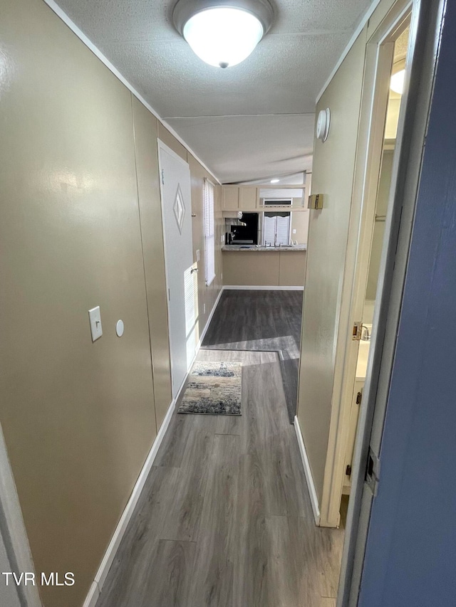 hall featuring crown molding, a textured ceiling, vaulted ceiling, and dark hardwood / wood-style flooring