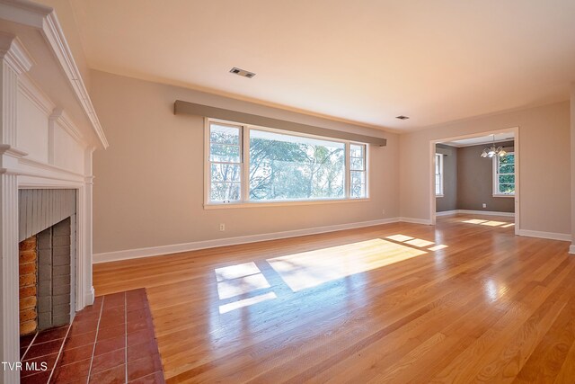 unfurnished living room with an inviting chandelier, hardwood / wood-style floors, a brick fireplace, and plenty of natural light