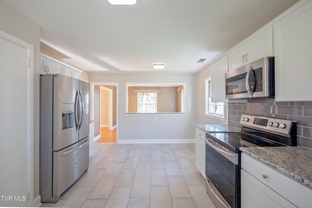 kitchen with stainless steel appliances, light stone countertops, white cabinetry, and backsplash