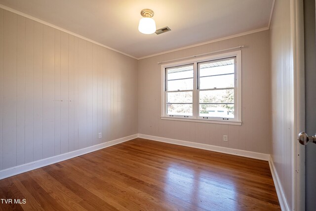 empty room featuring ornamental molding, wooden walls, and hardwood / wood-style flooring