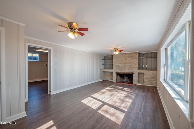 unfurnished living room with a stone fireplace, dark wood-type flooring, ceiling fan, and crown molding