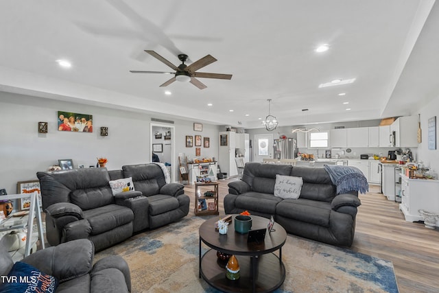 living room with light hardwood / wood-style floors and ceiling fan with notable chandelier