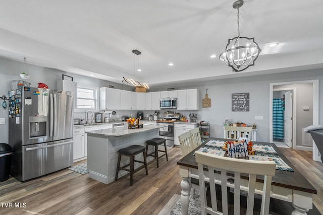 kitchen with appliances with stainless steel finishes, a kitchen island, dark hardwood / wood-style flooring, pendant lighting, and white cabinets