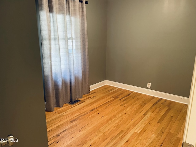 empty room with light wood finished floors, visible vents, and baseboards