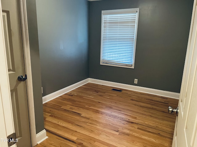 unfurnished room featuring baseboards, visible vents, and wood finished floors
