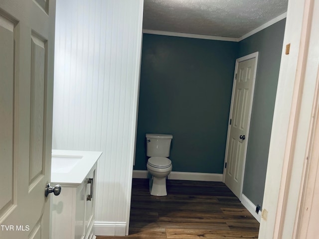 bathroom featuring toilet, wood-type flooring, ornamental molding, vanity, and a textured ceiling