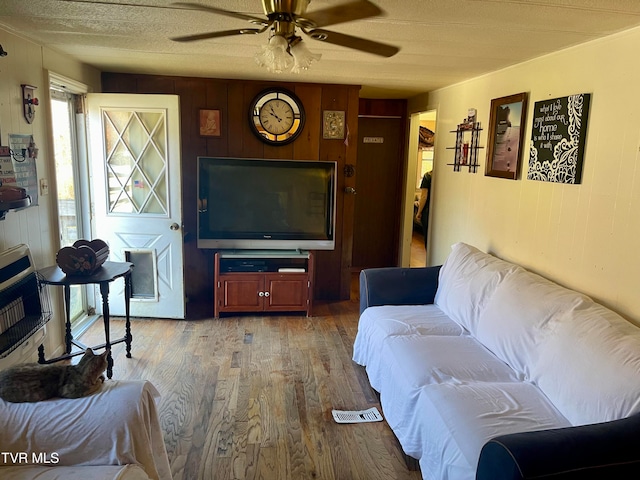 living room featuring hardwood / wood-style floors, ceiling fan, a textured ceiling, and wooden walls