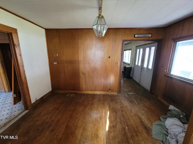 unfurnished dining area with an inviting chandelier, wood walls, and dark hardwood / wood-style flooring