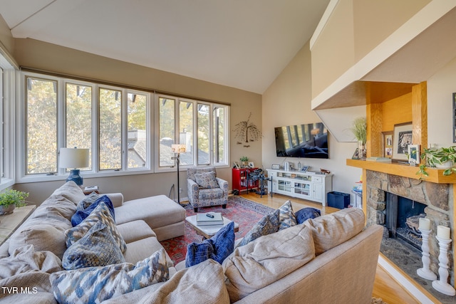 living room with light hardwood / wood-style flooring, vaulted ceiling, a stone fireplace, and a wealth of natural light