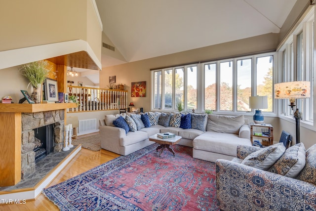 living room with high vaulted ceiling, hardwood / wood-style flooring, plenty of natural light, and a stone fireplace