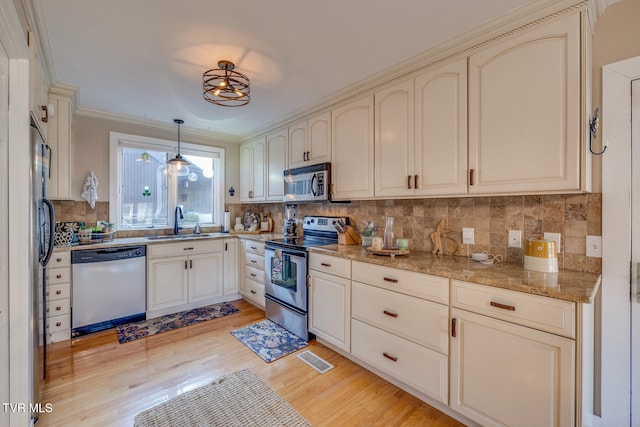 kitchen featuring light hardwood / wood-style flooring, crown molding, sink, decorative light fixtures, and appliances with stainless steel finishes