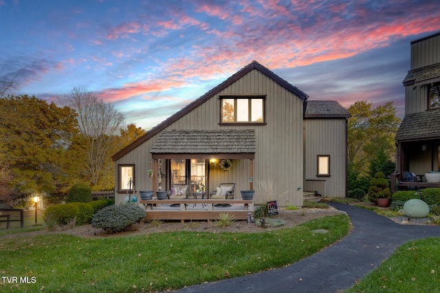 back house at dusk featuring a deck and a lawn