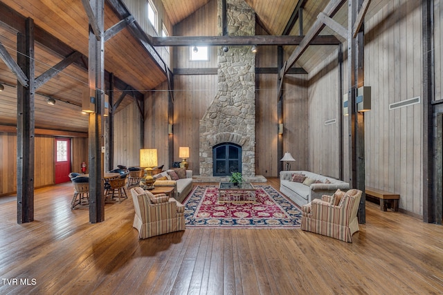 living room featuring a stone fireplace, hardwood / wood-style floors, wooden ceiling, wooden walls, and high vaulted ceiling