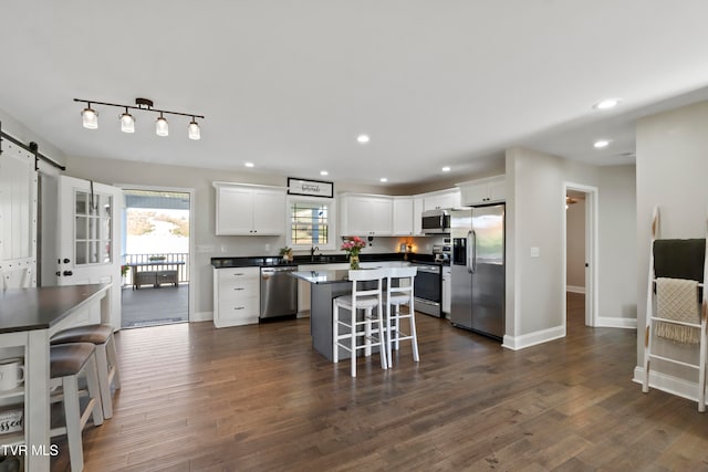 kitchen with a barn door, a center island, dark hardwood / wood-style flooring, a kitchen breakfast bar, and stainless steel appliances