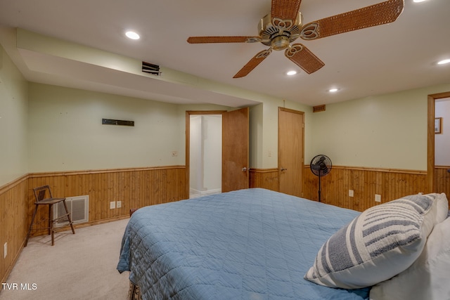 bedroom with ceiling fan, light carpet, and wood walls